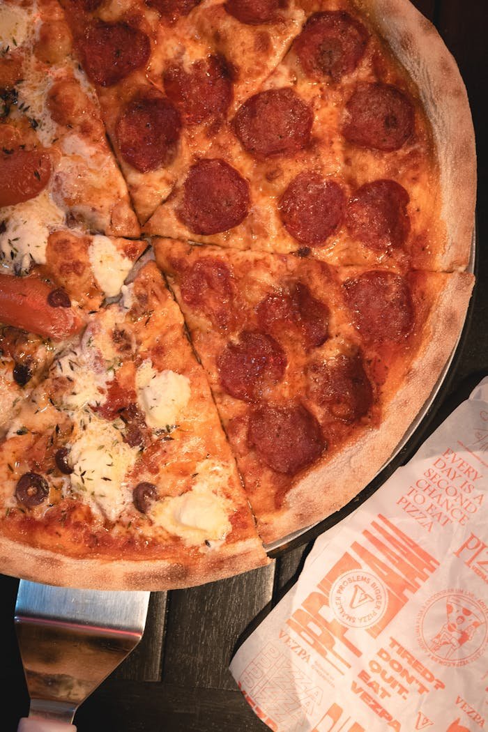 Close-up of a sliced pepperoni pizza with vibrant toppings on a dark surface.